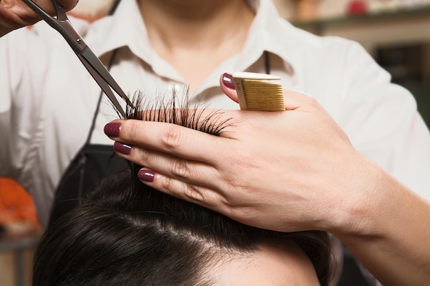 Обрезанный снимок женщины-парикмахера, стригущей мужские волосы ножницами в парикмахерской. Избавьтесь от этих секущихся кончиков.