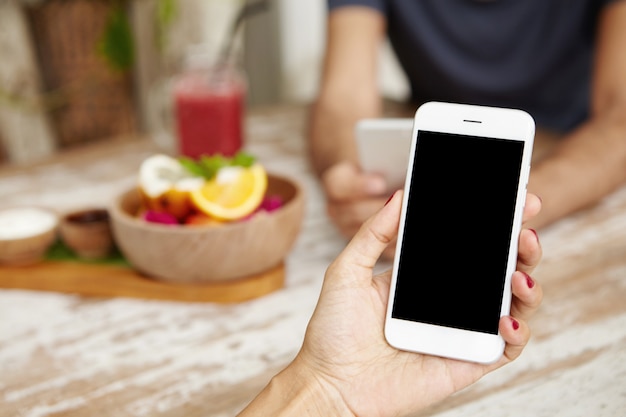 Cropped shot of female hand with red nails reading message via email or making call on generic smart phone, having lunch with her husband