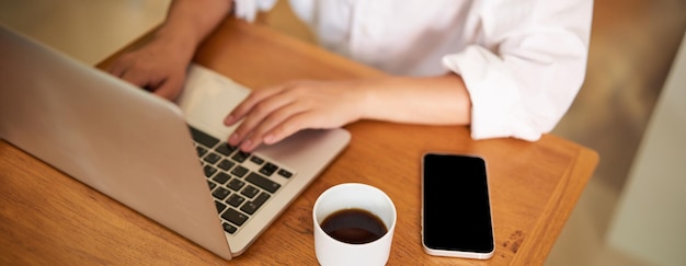 Cropped shot of female hands typing on laptop keyboard drinking coffee working in cafe studying