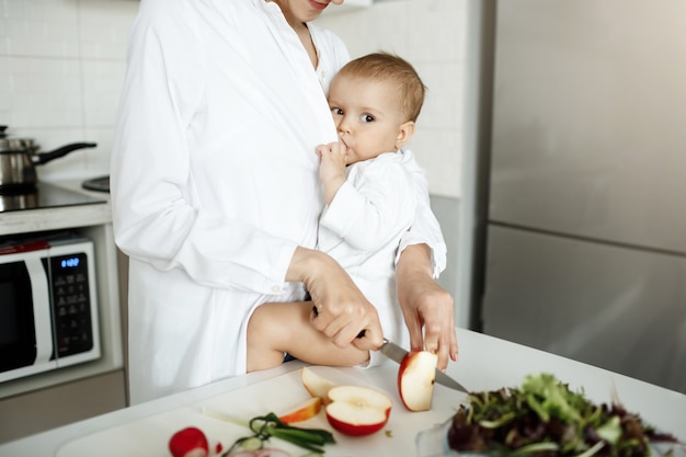 Free photo cropped shot of mother breastfeeding her baby while slicing an apple