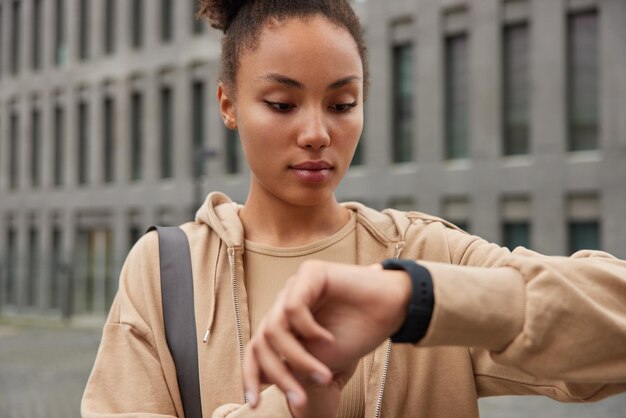 Cropped shot of serious fitness model looks at digital smartwatch device checks results after training in gym wears casual beige sweatshirt has regular exercising outdoors. People sport motivation
