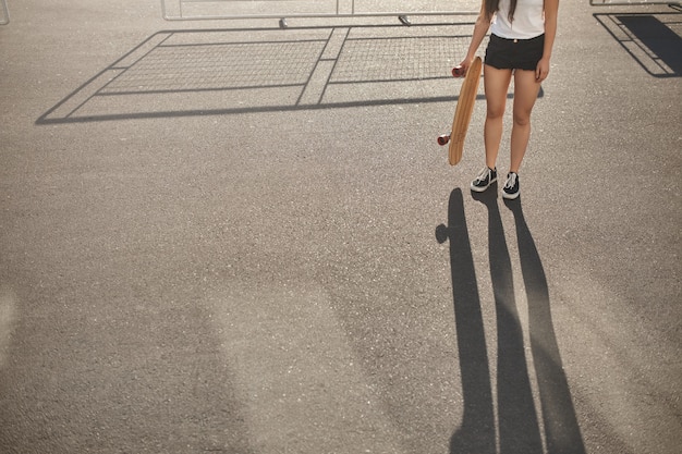 Cropped shot skater girl in shorts, sneakers riding practicing skateboarding