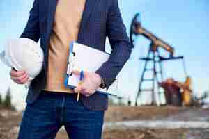 Free photo cropped snapshot of an inspector in oil field holding folder for notes and a helmet