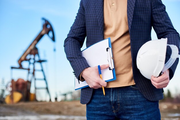 Cropped snapshot of an inspector in oil field holding folder for notes and a helmet