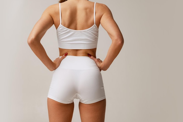 Cropped studi image of slim fit female body in white cotton underwear posing isolated over beige background Back view