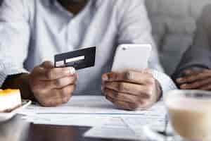 Free photo cropped view of african-american businesman holding mobile phone and credit card while paying bill at cafe