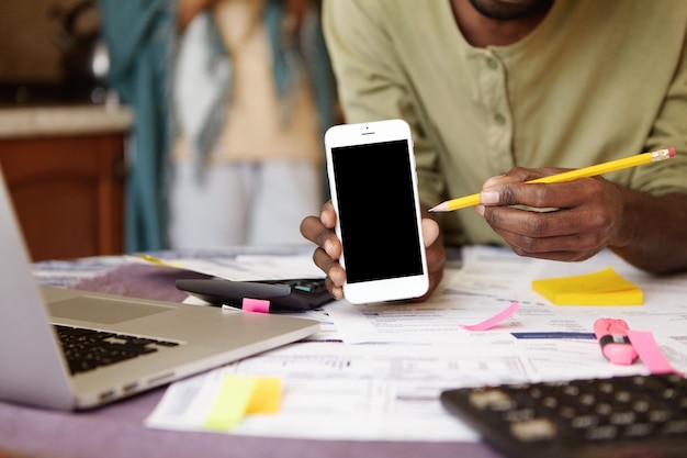 Cropped view of casual African-American man pointing pencil at blank screen of mobile phone