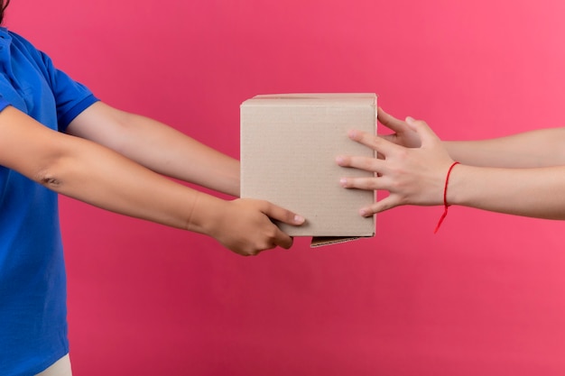 Free photo cropped view of delivery girl giving box package to a customer over isolated pink space