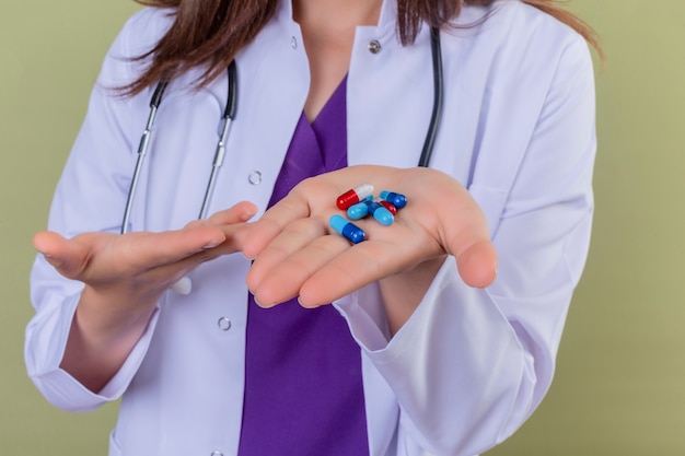 Cropped view of woman doctor in white coat presenting pills in arm on isolated green