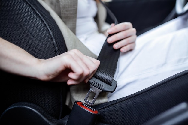 Cropped view of woman fastening safety belt while sitting in car on blurred foreground Cut view of young woman's hands locking seat belt in car Sitting alone Close up