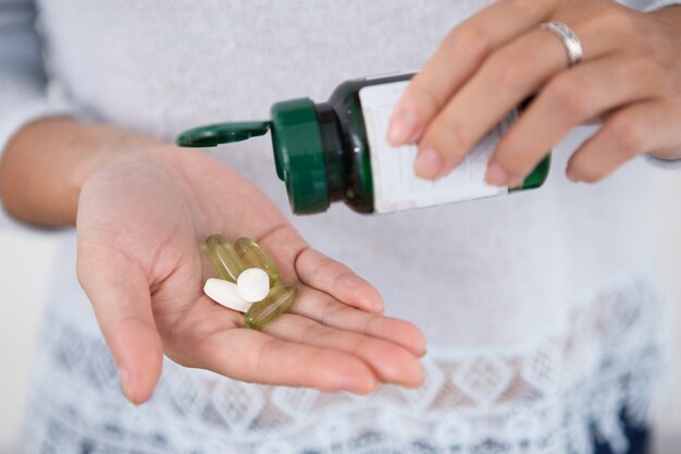 Обрезанный вид женщины, выливая таблетки из бутылки