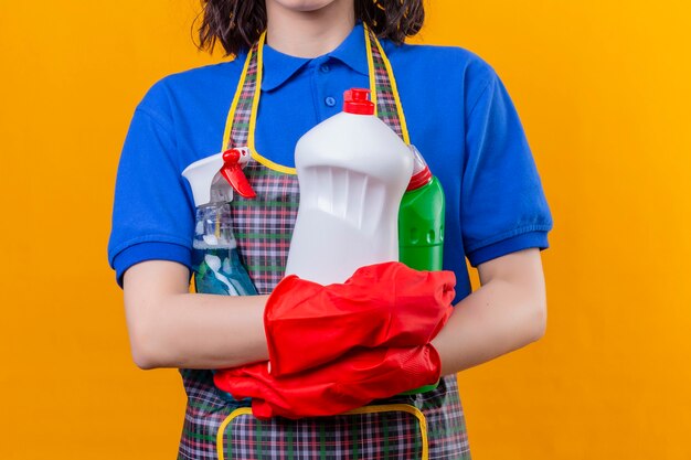 Cropped view of woman wearing apron and rubber gloves holding cleaning supplies  space