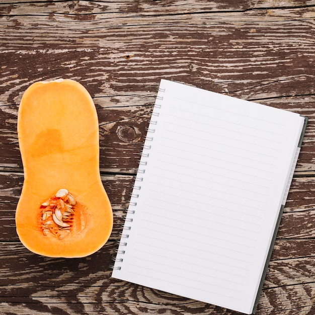 Cross section of butternut squash and spiral notepad on wooden desk