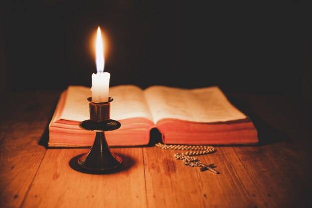 Cross with bible and candle on a old oak wooden table. Beautiful gold background.