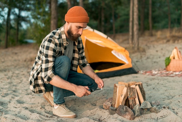 Crouching hipster lighting campfire