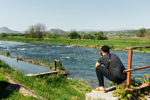 Free photo crouching man taking photo of idyllic river