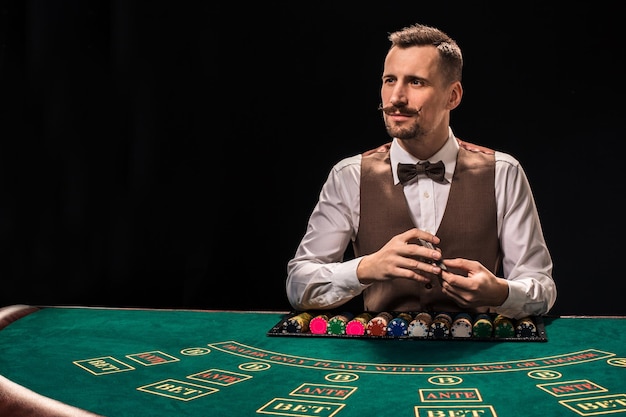 Croupier behind gambling table in a casino on black background. The concept of victory.