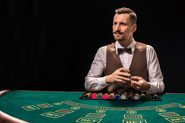 Croupier behind gambling table in a casino on black background. The concept of victory.