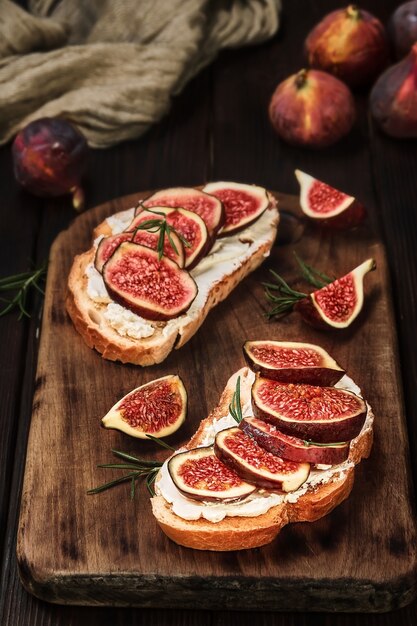 Croutons with figs and cream cheese on a wooden board, closeup view, selective focus. Snack idea. Close-up on healthy food