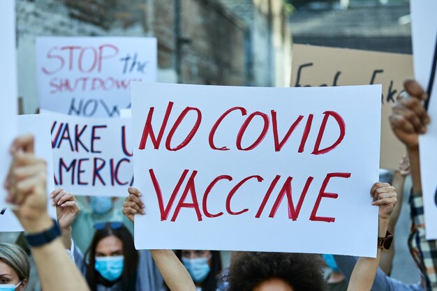 Crowd of people carrying banners while protesting against coronavirus vaccination on city streets