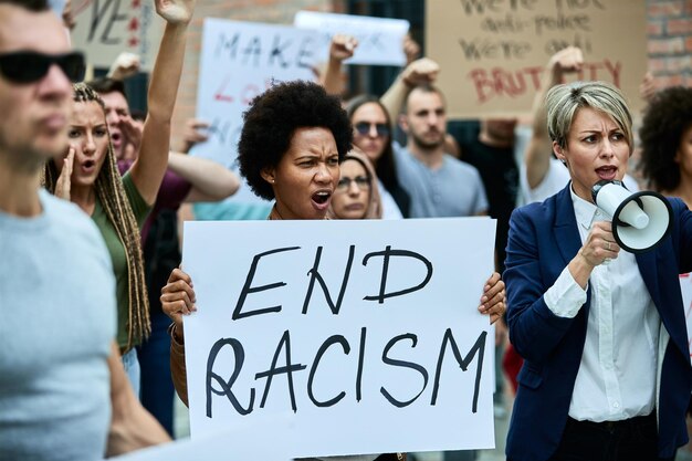 路上で人種差別に抗議する人々の群衆焦点は、エンド人種差別の碑文のバナーを保持しているアフリカ系アメリカ人の女性にあります