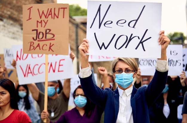 Folla di persone che indossano una maschera protettiva e protestano dopo aver perso il lavoro a causa della pandemia di coronavirus