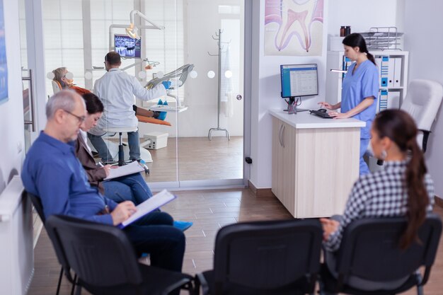 Crowded stomatology waiting area with people filling form for dental consultation