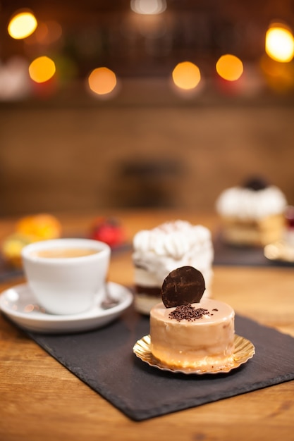 Free photo crumbles of chocholate on a tasty dessert with biscuit on top over a wooden table near a delicious coffee. mini cake baked after traditional recipe.