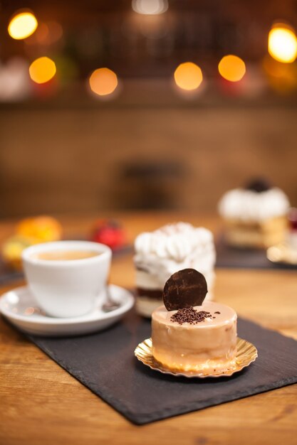 Crumbles of chocholate on a tasty dessert with biscuit on top over a wooden table near a delicious coffee. Mini cake baked after traditional recipe.