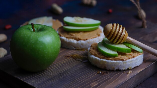 떡 빵과 녹색 사과 조각과 꿀 바삭 바삭한 천연 땅콩 버터 샌드위치.