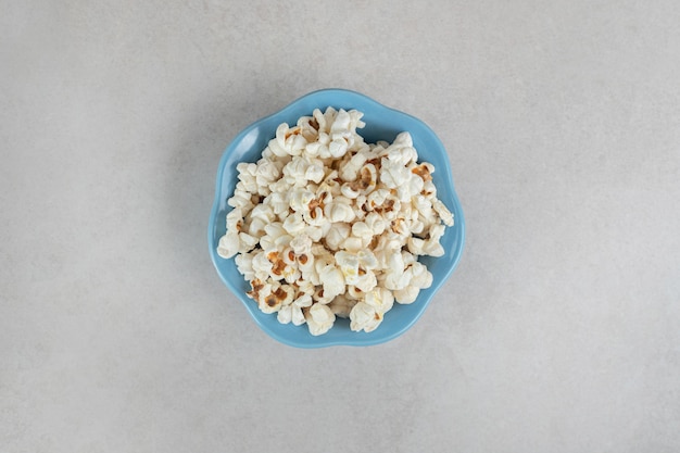 Crunchy popcorn in a small blue bowl on marble.
