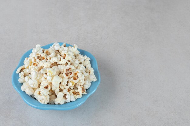 Crunchy popcorn on a small blue platter on marble table.