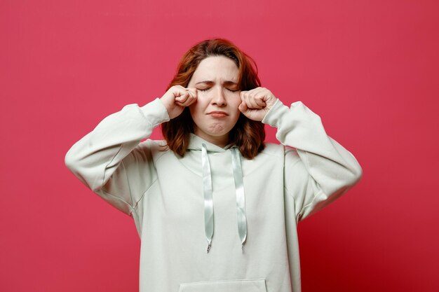 Crying wiping face young beautiful girl in white sweater isolated on pink background