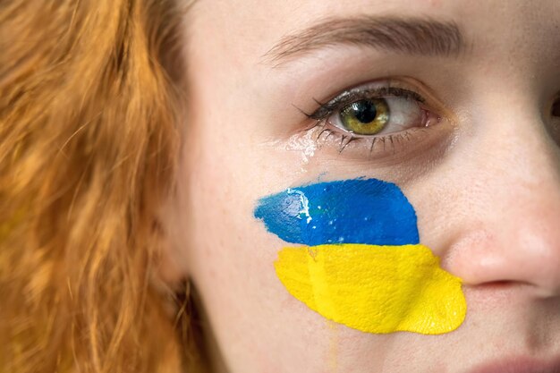 彼女の頬にウクライナの国旗を持つ泣いている女性