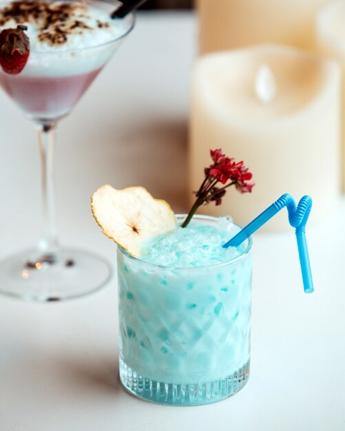 A crystal glass of blue cocktail garnished with dried pear slice