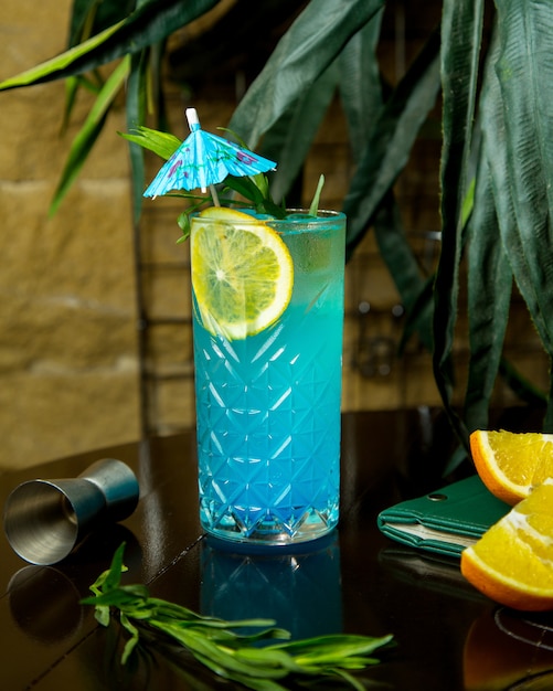 A crystal glass of blue lagoon garnished with lemon slice and cocktail umbrella