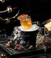 Free photo crystal glass of cold cocktail garnished with dried orange slice served in smoked bucket