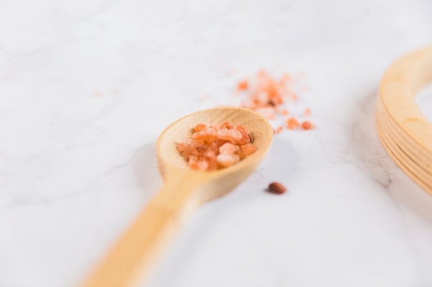 Crystal of himalayan salt on wooden spoon over the marble backdrop