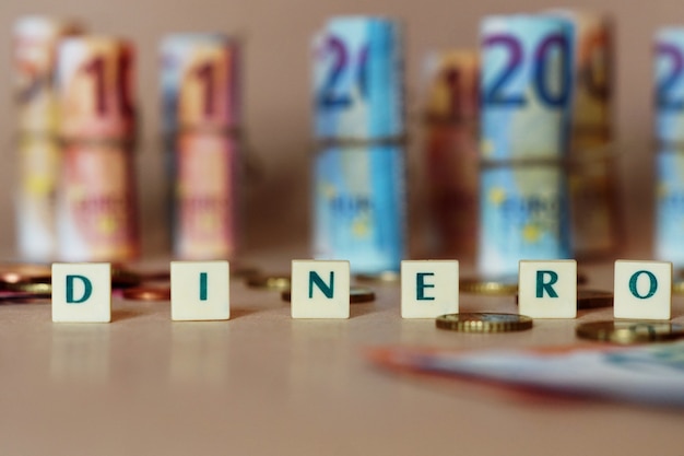 テーブルの上のスペインのdinero紙幣と硬貨の前でDineroを綴る立方体