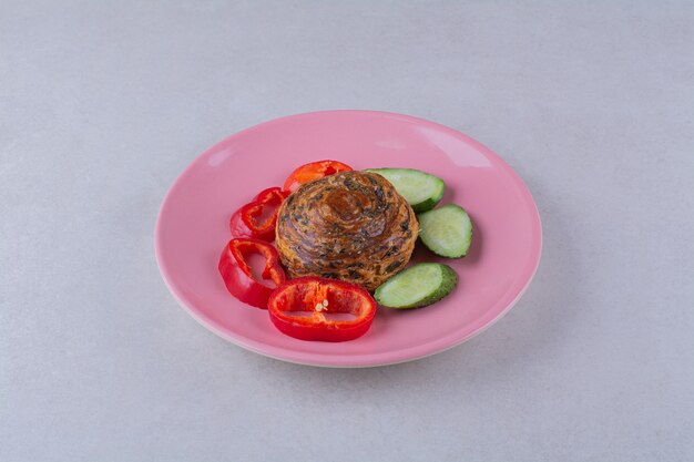 Cucumber and pepper slices around the cookie on plate on the dark surface