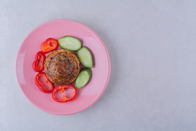 Cucumber and pepper slices around the cookie on plate on marble table.