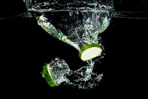 Cucumber slices splashing into water over the black background