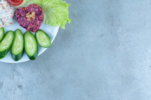 Cucumber and tomato slices with lettuce garnishing two salads on a platter on marble table.