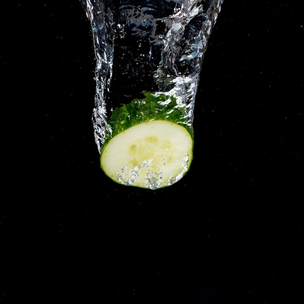 Cucumber with water splash falling on black background