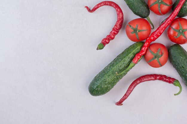 Cucumbers, chili peppers and tomatoes on white surface