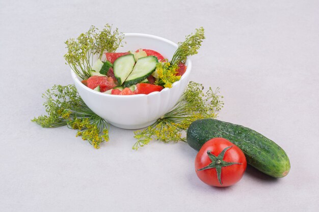 Cucumbers and tomato salad with greens on white surface