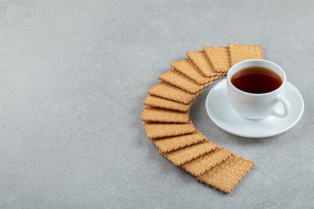 A cup of aroma tea with crackers on a gray background .