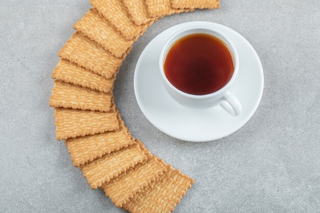 A cup of aroma tea with crackers on a gray surface .