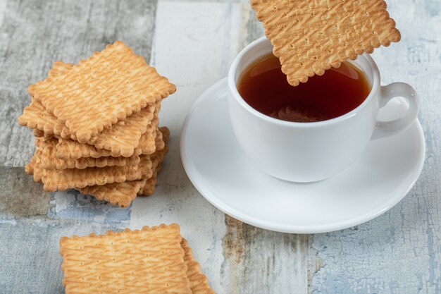 A cup of aroma tea with crackers on a wooden table.