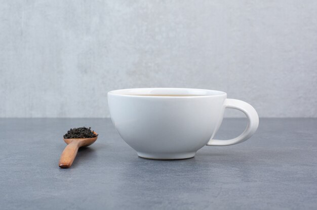 A cup of aroma tea with wooden spoon of infusion .
